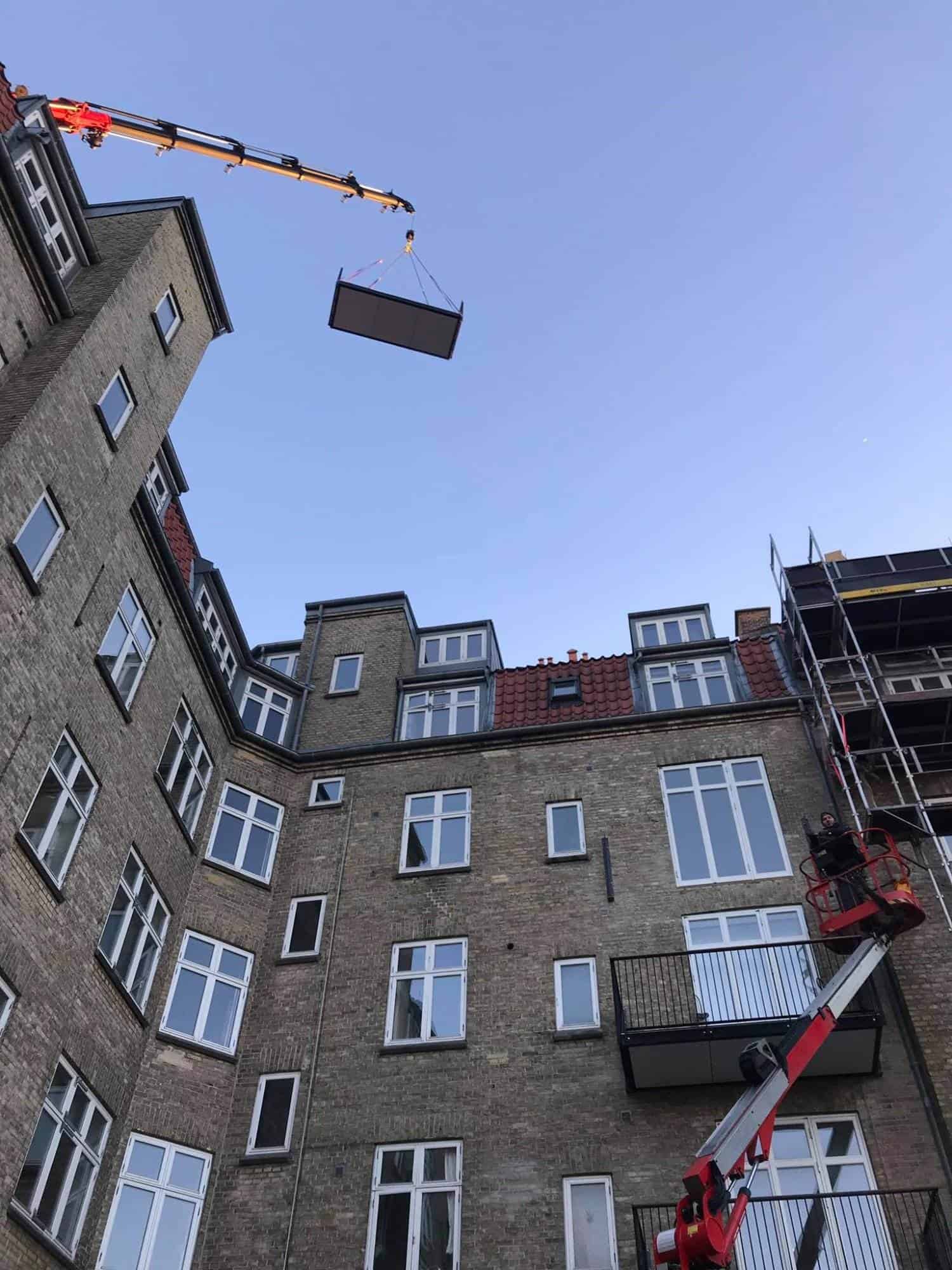 Kran løfter en stor betonplade til en renovering af en boligblok.