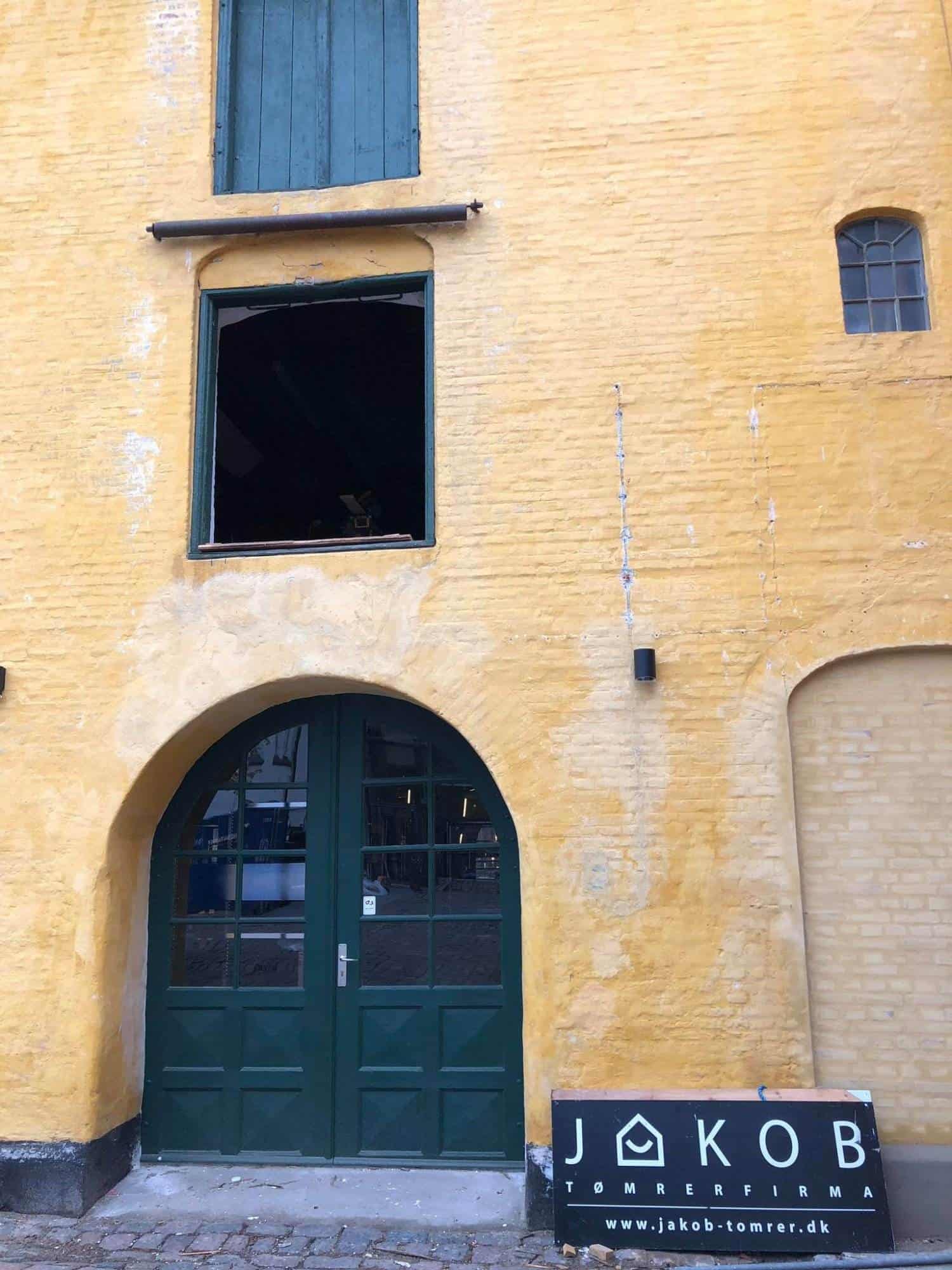 Gammel murstensbygning med grøn dør og vinduer.