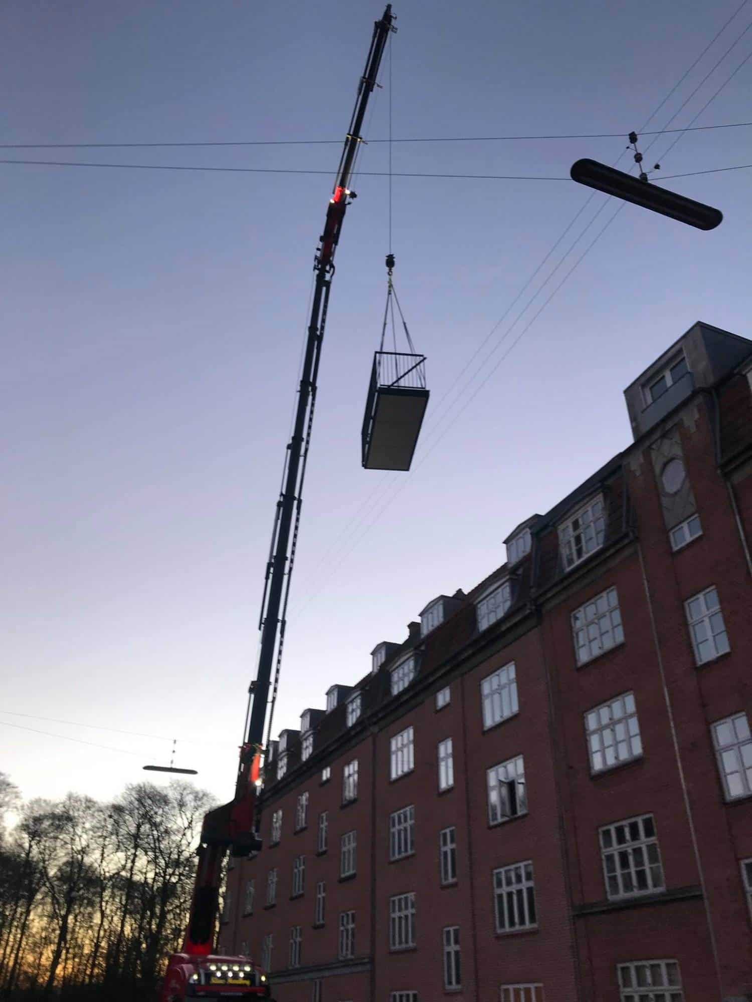 Kran løfter container til byggeri på en bygningsfacade i København.