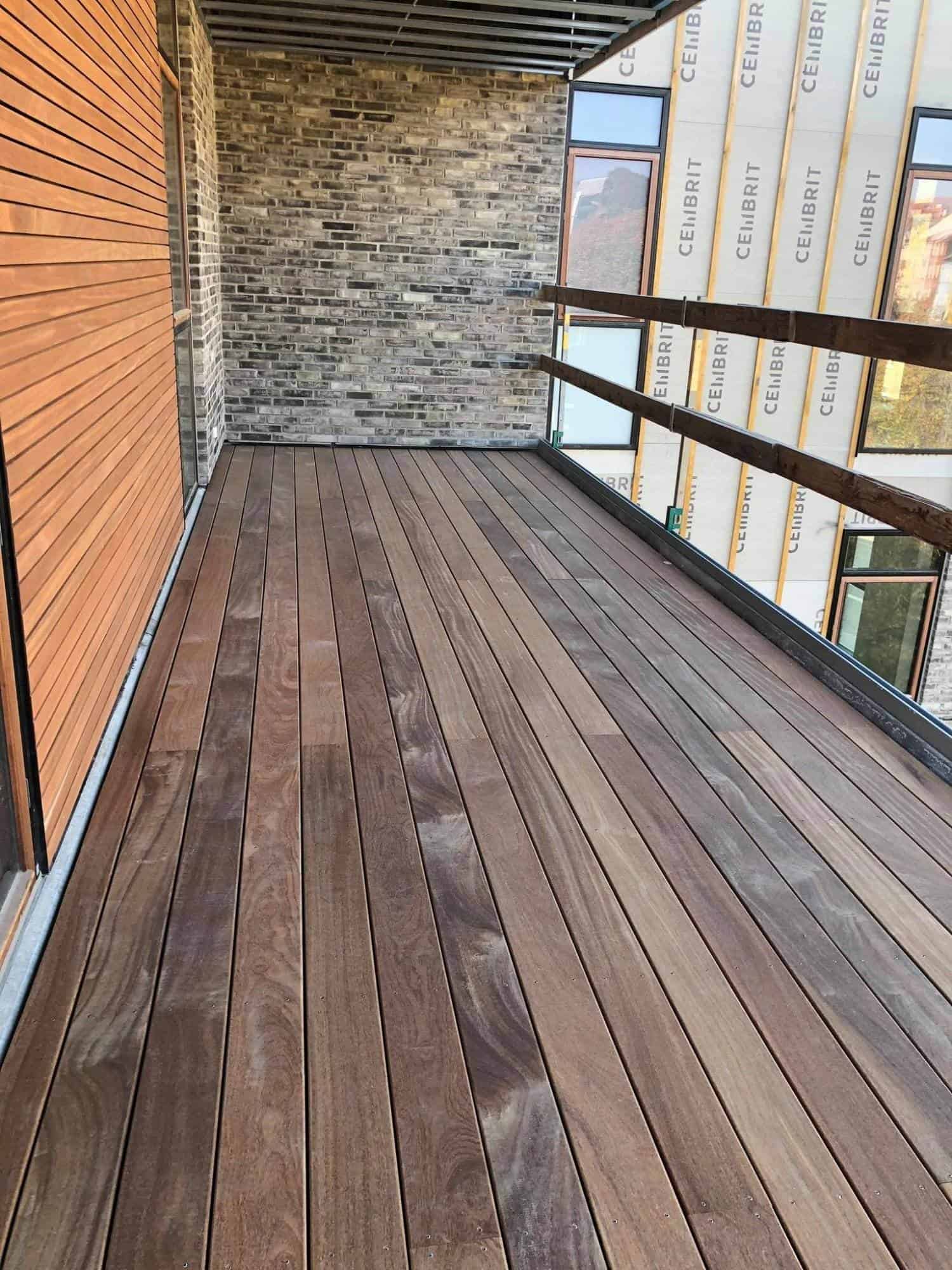 Udendørs trædæk med glasræling på balkon, moderne bygning.