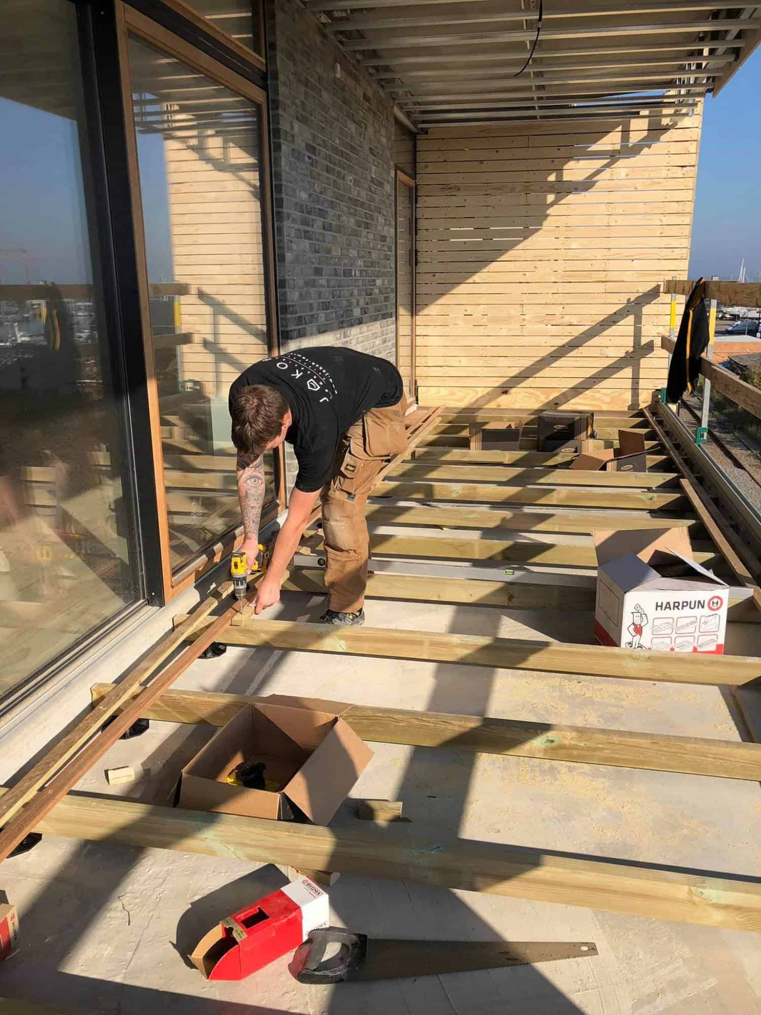 Tømrer arbejder på altan med trærammer og værktøj.