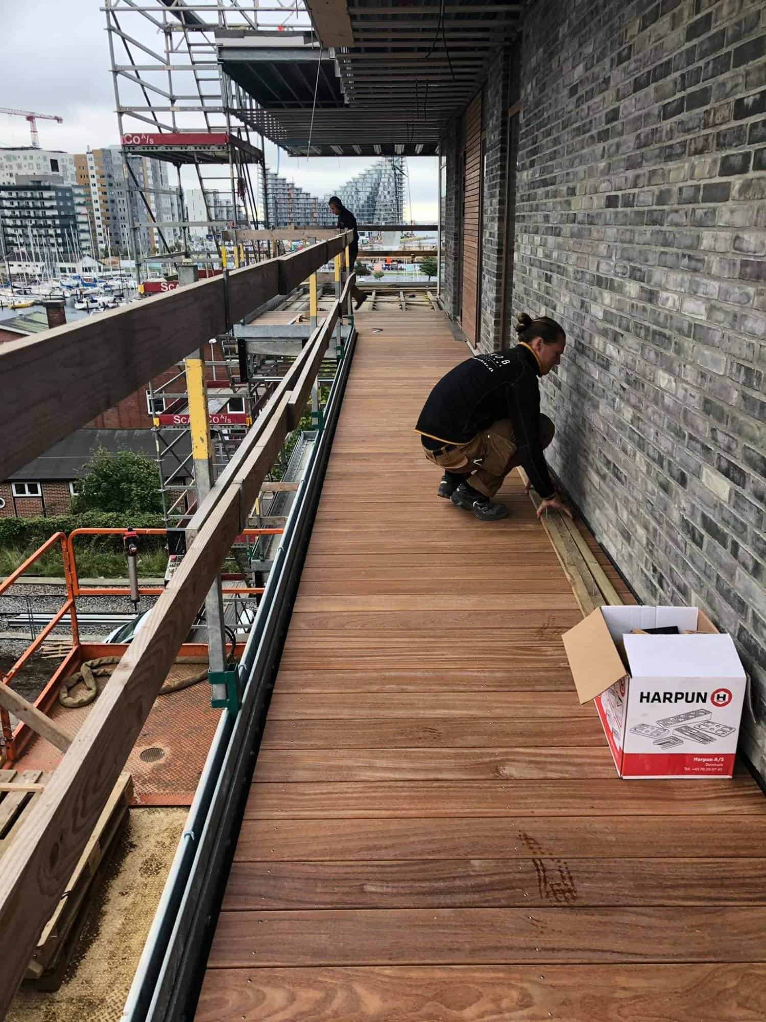 Tømrerarbejde på udendørs altan med træplanker og sikkerhedsbarrierer.