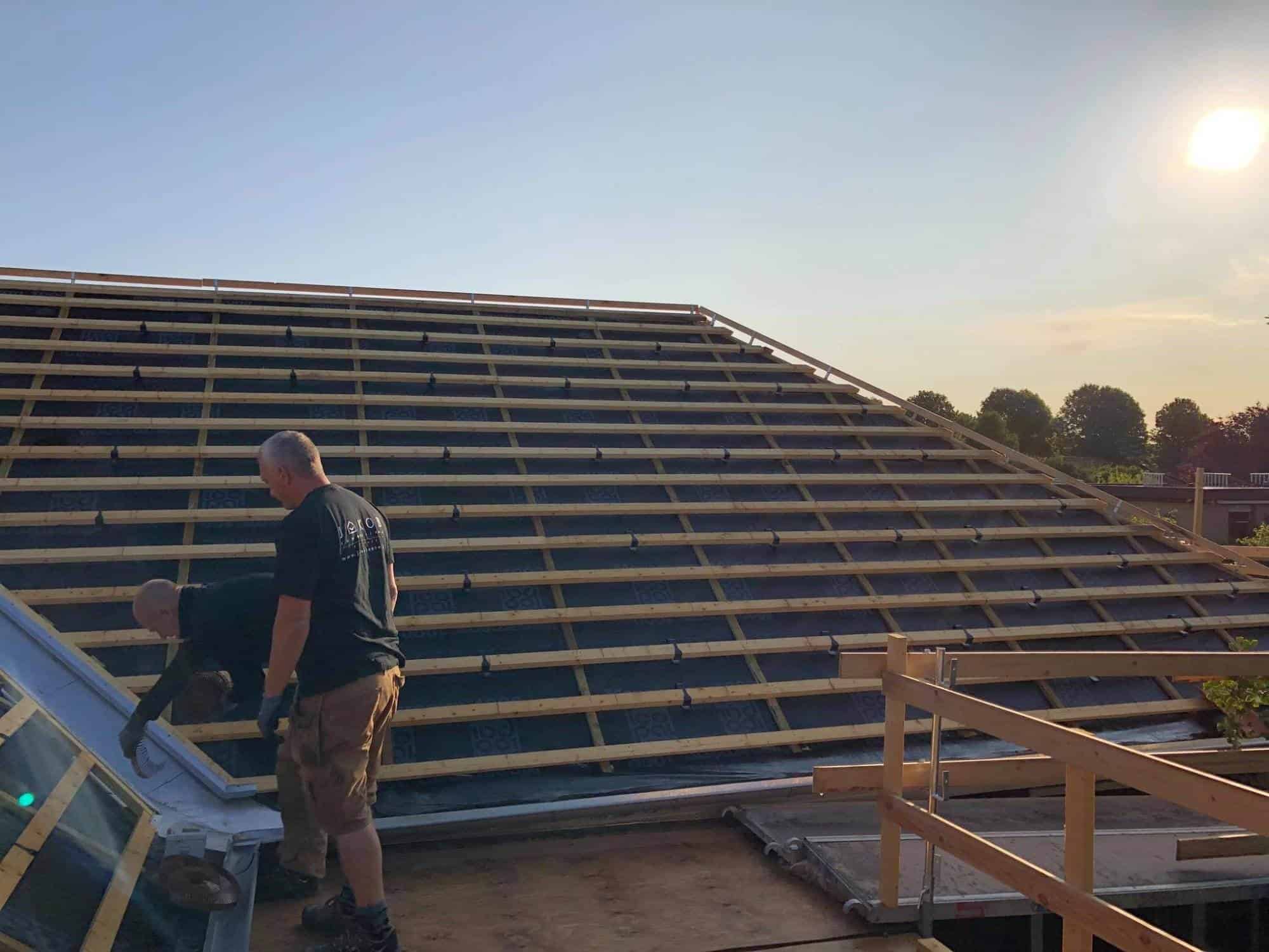 Tømrer arbejder på tagkonstruktion med træspær i solnedgang.