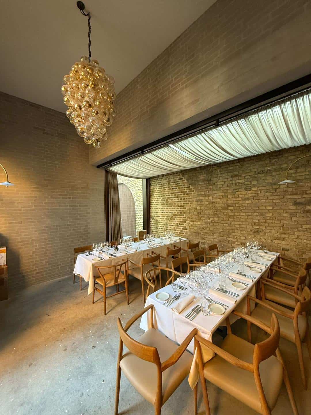 Elegant selskabslokale med langbord, moderne belysning og rustikke vægge.