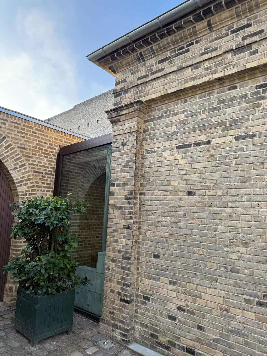 Gammel murstensvæg med nyt træværk og planter foran.