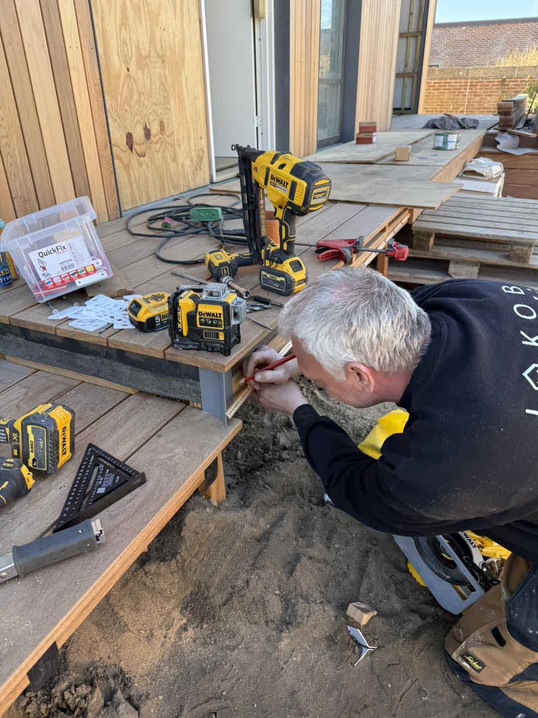 Håndværker monterer træterrasse med værktøj og materialer.