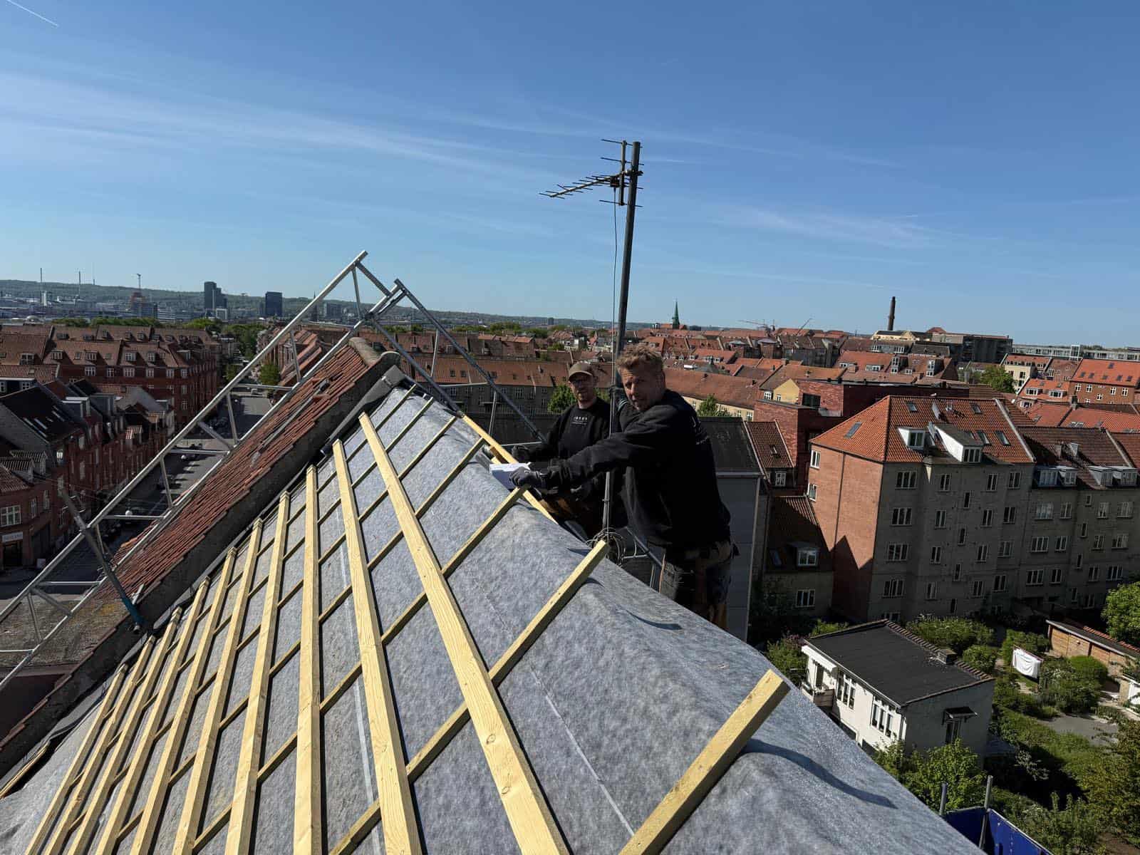Tømrere arbejder på tagrenovering med træspær og tagpap i København.
