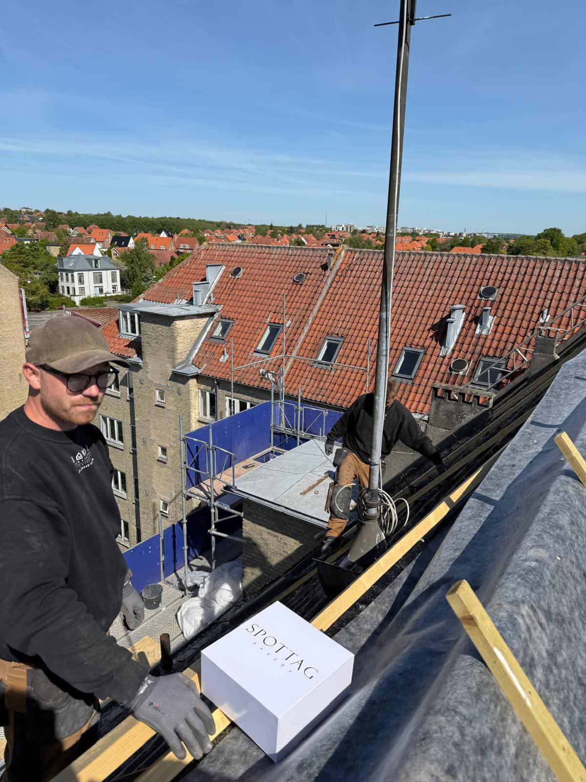 Billede af tømrer, der arbejder på tagkonstruktion med udsigt over byen.