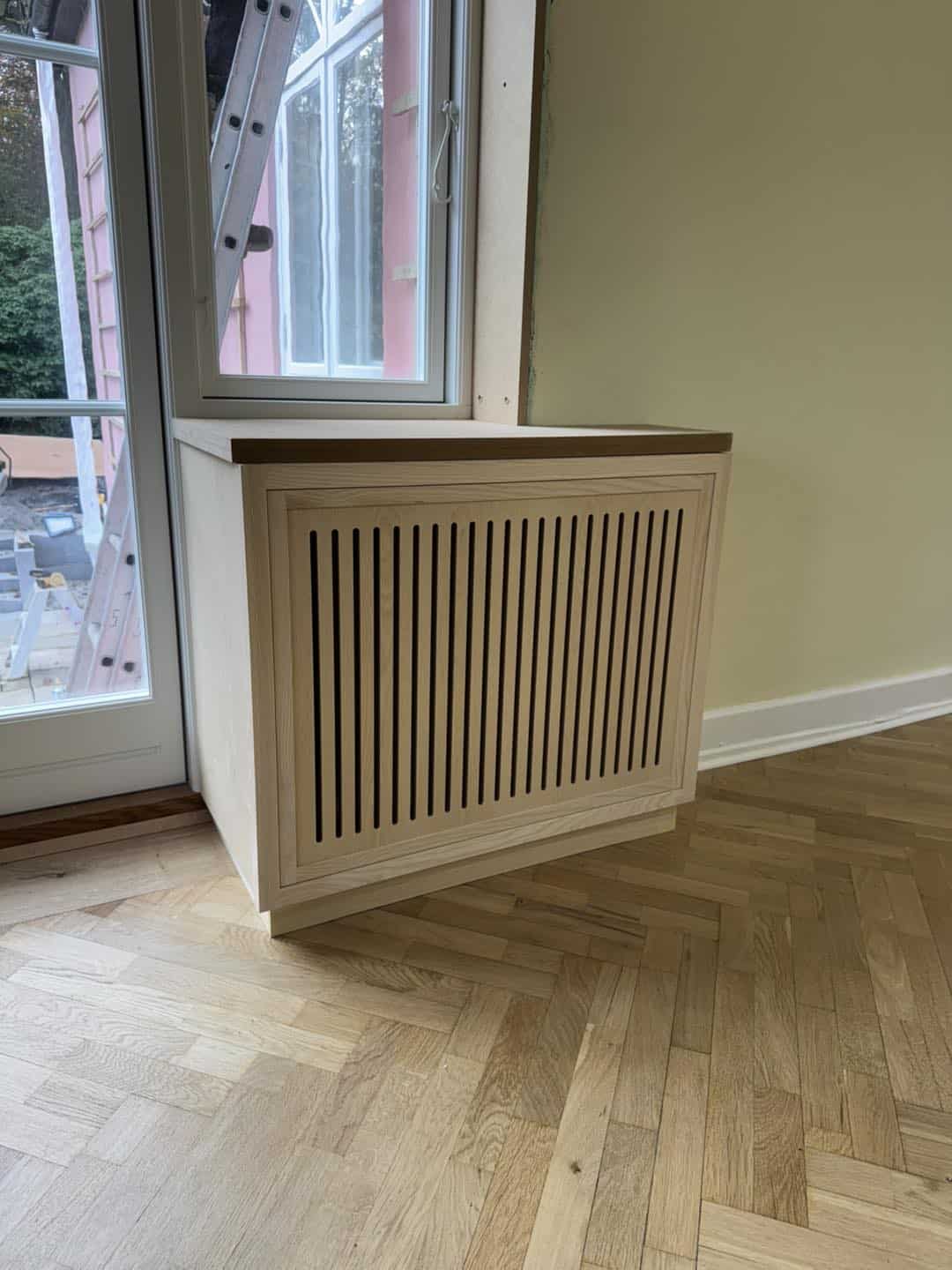 Hjørneskab med ventilationsgitter foran vindue.