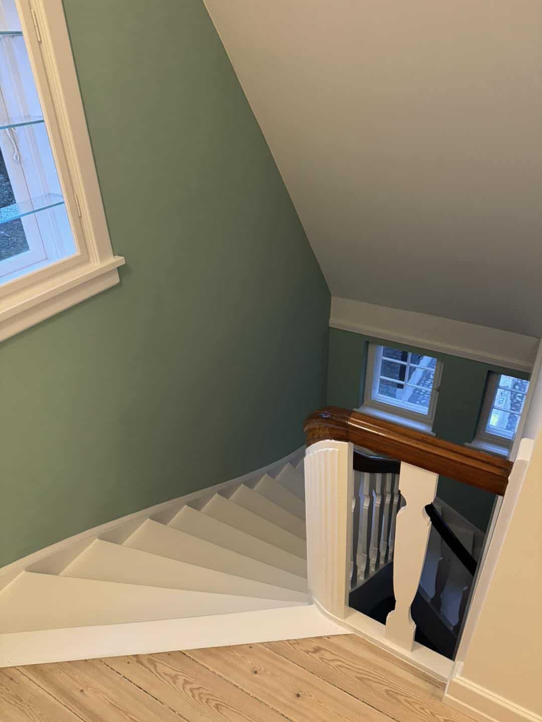 Trappe til første sal med hvidt gelænder og trægulv, underetagen med grøn væg.