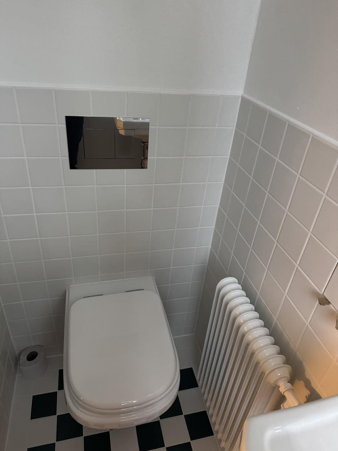 Moderne toilet med vægskjult cistern og radiator i badeværelse.