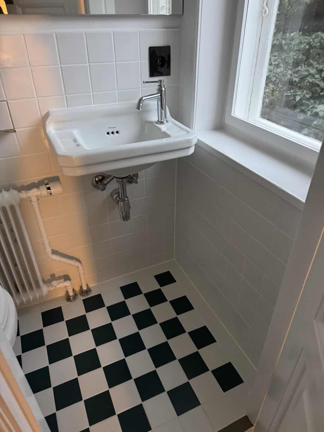 Lille vask på væg med sort-hvidt flisegulv, perfekt til små badeværelser.