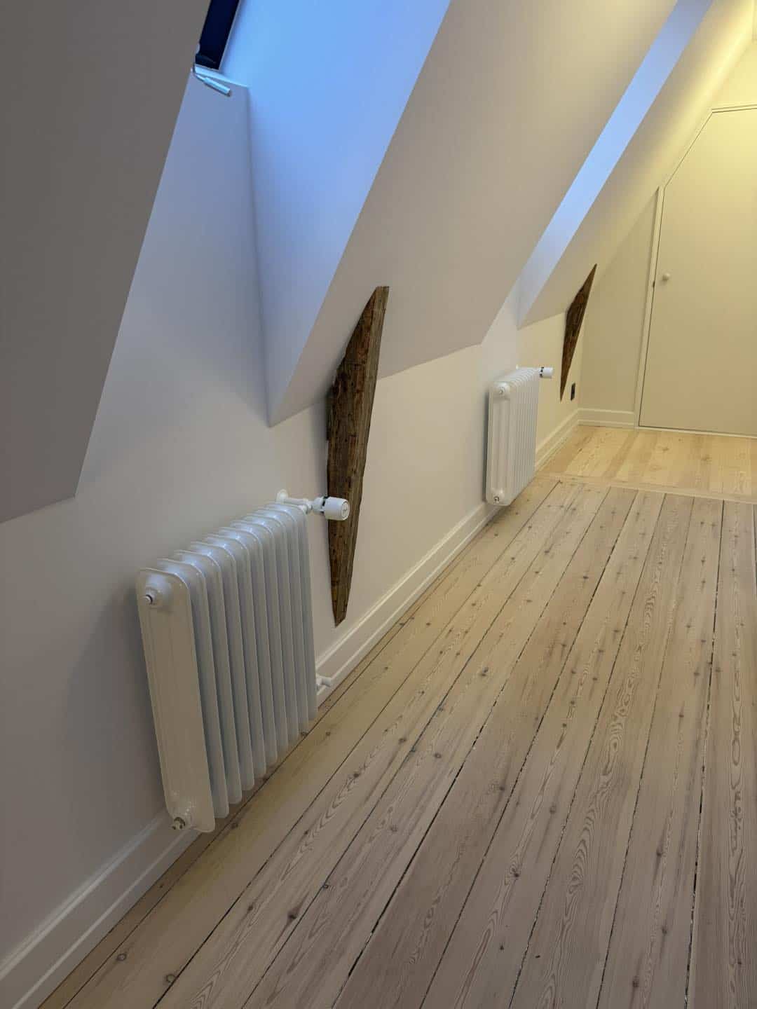 Indvendigt træværk og radiator under skrå væg i et lyst rum.